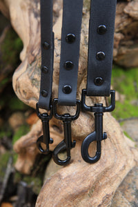 Three Black Henry & Sadie Leashes with black hardware hanging next to a curved light log with a blurred forest background