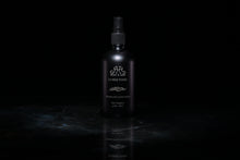 Load image into Gallery viewer, A dark matte spray bottle of La Mer Noire Room and Linen Spray, standing on a reflective dark surface against a solid black background.
