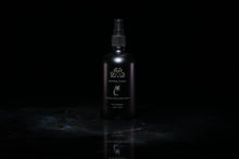 Load image into Gallery viewer, A matte black spray bottle of Santal Coco Room and Linen Spray, standing upright on a dark reflective surface against a solid black background.