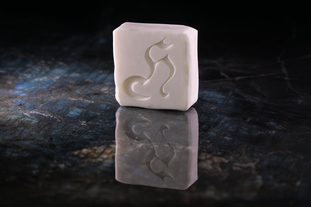 A rectangular white soap bar with a carved stylized Henry & Sadie silhouette, standing upright on a dark reflective surface against a black background.
