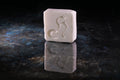 A rectangular white soap bar with a carved stylized Henry & Sadie silhouette, standing upright on a dark reflective surface against a black background.