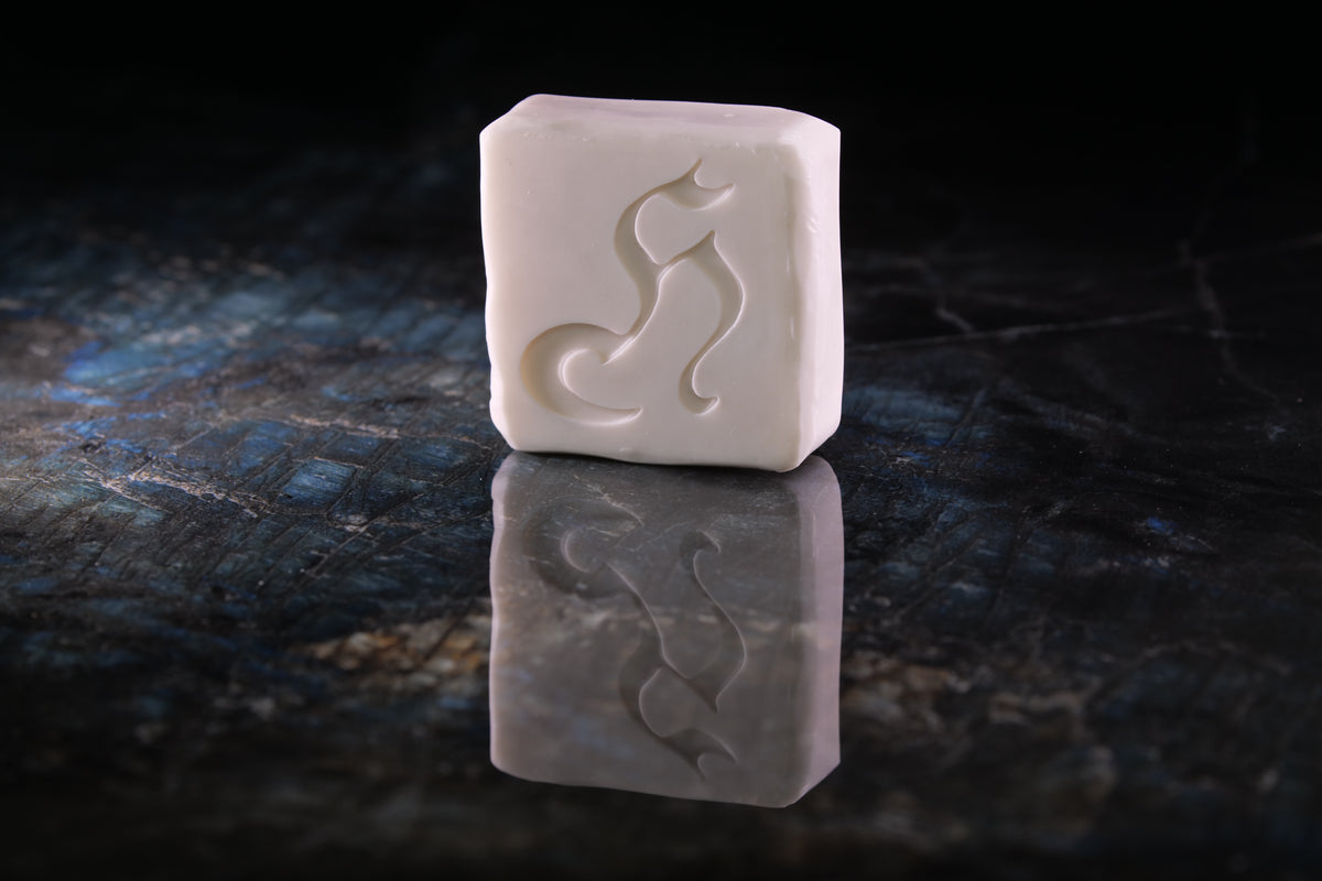 A rectangular white soap bar with a carved stylized cat silhouette, standing upright on a dark reflective surface against a black background.