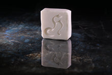 Load image into Gallery viewer, A rectangular white soap bar with a carved stylized cat silhouette, standing upright on a dark reflective surface against a black background.