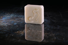 Load image into Gallery viewer, A rectangular cream-colored soap bar with an embossed cat silhouette, standing on a dark reflective surface against a dark background.