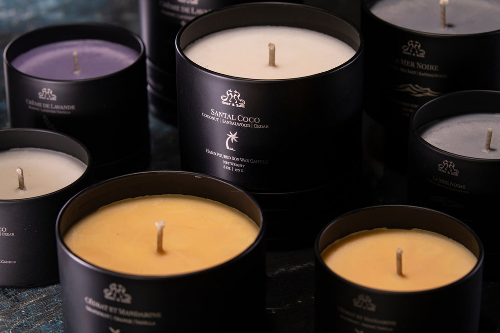 An assortment of candles with gray, pale yellow, lavender, and white wax arranged with the "Santal Coco" candle in the center in a black tin