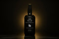 A black room and linen spray bottle standing against a dark background with a warm spotlight glow behind it. The bottle features white text and a small white mandarin fruit illustration, with the Henry & Sadie brand 'Cédrat et Mandarine' visible.