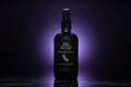 A black spray bottle of Henry & Sadie Crème de Lavande room and linen spray, illuminated by a purple glow against a dark background.