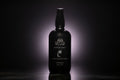 A matte black spray bottle of Santal Coco Room and Linen Spray, centered against a dark background with a soft  glow behind it.