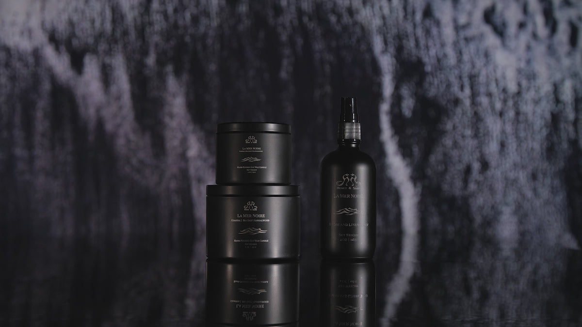 Video showing the Henry & Sadie La Mer Noire Room Spray and Candles in black containers on a reflective black surface with white and black waves crashing in the background